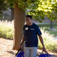 GVSU Alumni carrying two blue duffle bags into dorm